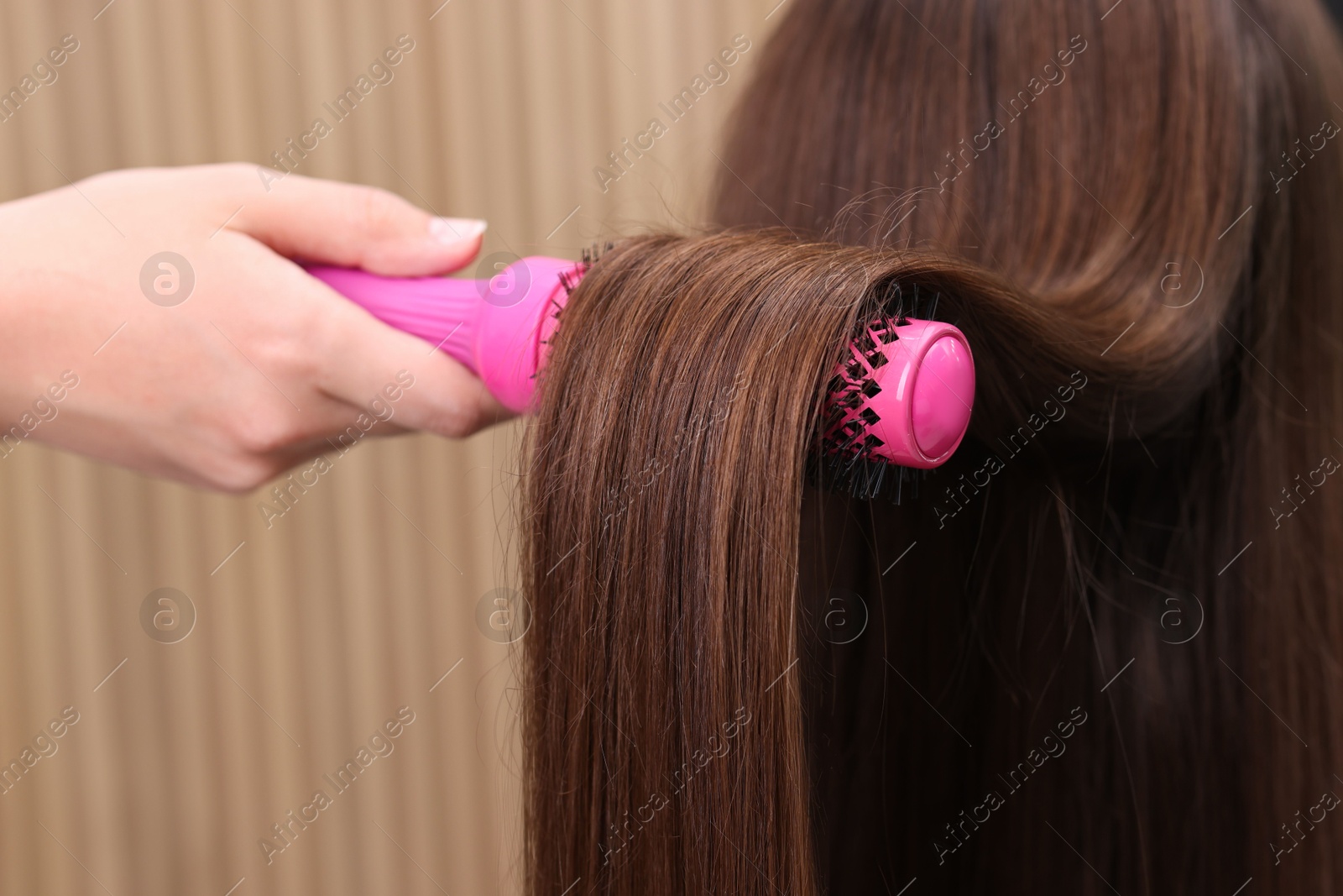 Photo of Hairdresser styling client's hair with round brush in salon, closeup