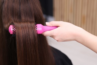 Photo of Hairdresser styling client's hair with round brush in salon, closeup