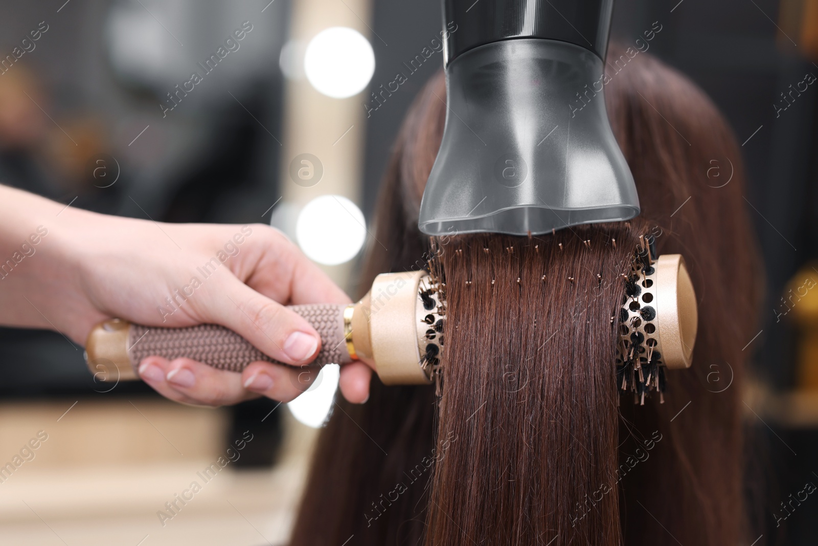 Photo of Hairdresser styling client's hair with round brush and hairdryer in salon, closeup