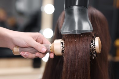 Photo of Hairdresser styling client's hair with round brush and hairdryer in salon, closeup