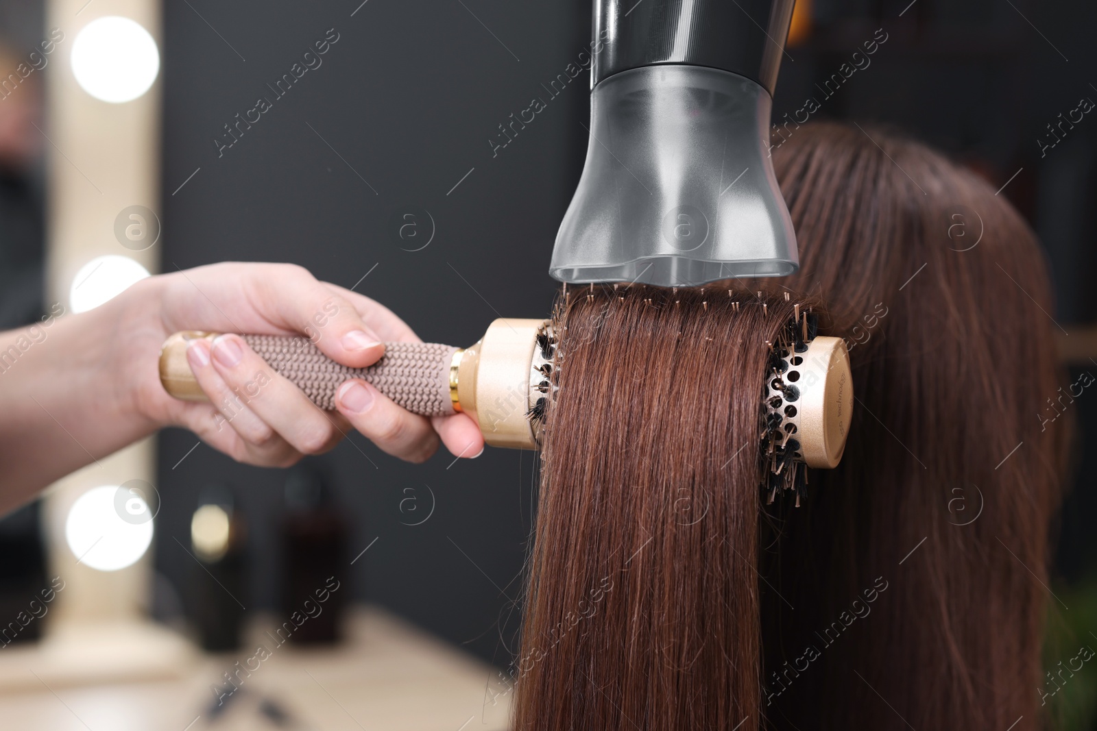 Photo of Hairdresser styling client's hair with round brush and hairdryer in salon, closeup