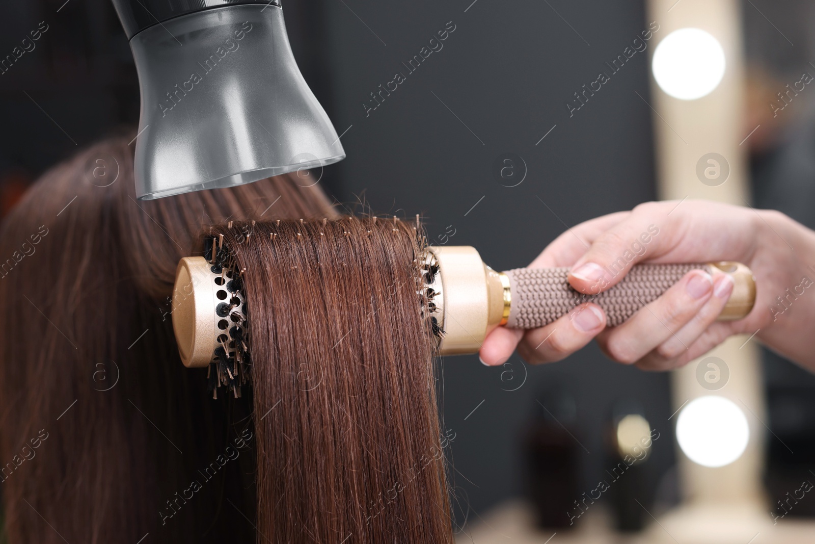 Photo of Hairdresser styling client's hair with round brush and hairdryer in salon, closeup