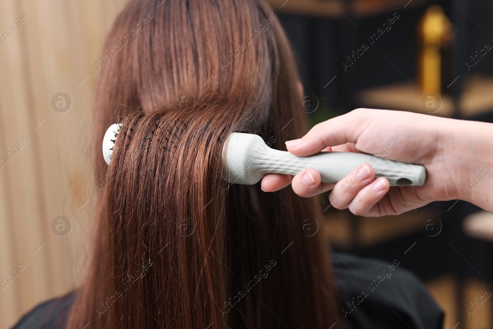 Photo of Hairdresser styling client's hair with round brush in salon, closeup