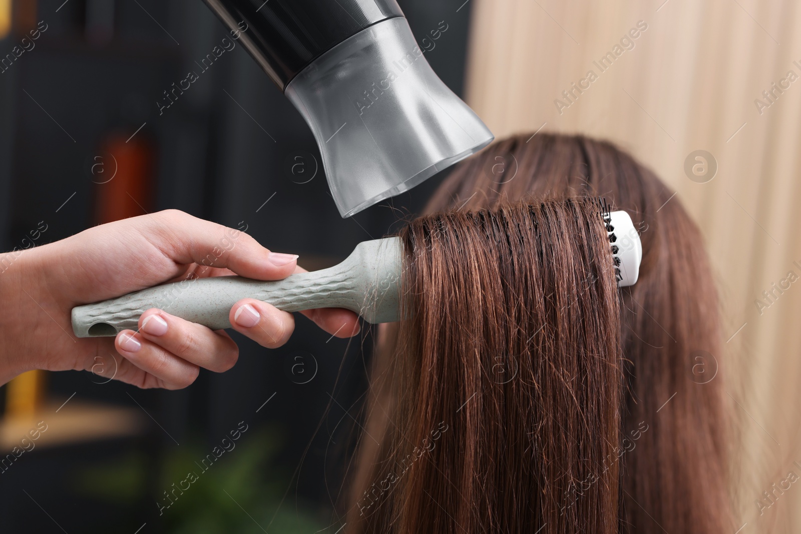 Photo of Hairdresser styling client's hair with round brush and hairdryer in salon, closeup