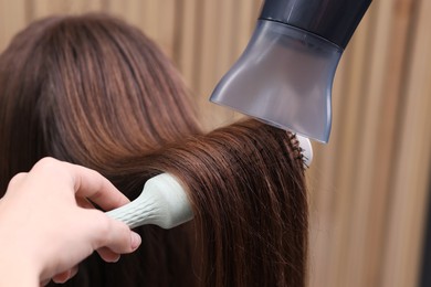 Photo of Hairdresser styling client's hair with round brush and hairdryer in salon, closeup