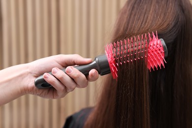 Photo of Hairdresser styling client's hair with round brush in salon, closeup