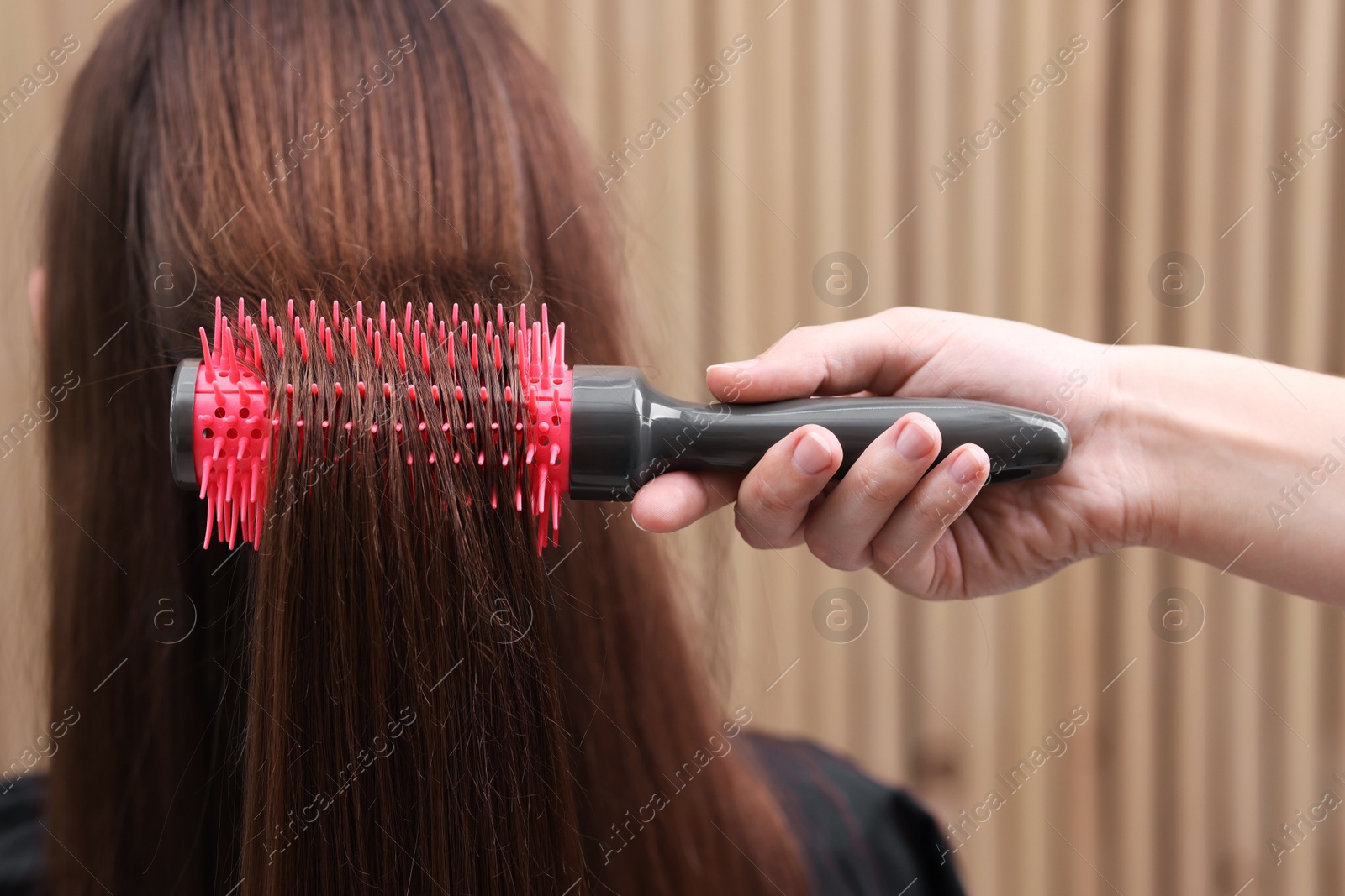 Photo of Hairdresser styling client's hair with round brush in salon, closeup