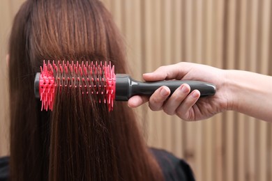 Photo of Hairdresser styling client's hair with round brush in salon, closeup