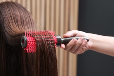 Photo of Hairdresser styling client's hair with round brush in salon, closeup