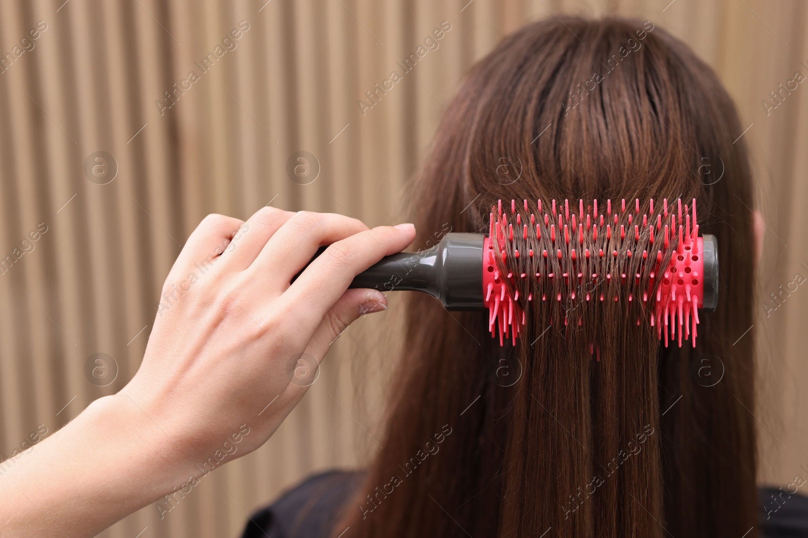 Photo of Hairdresser styling client's hair with round brush in salon, closeup