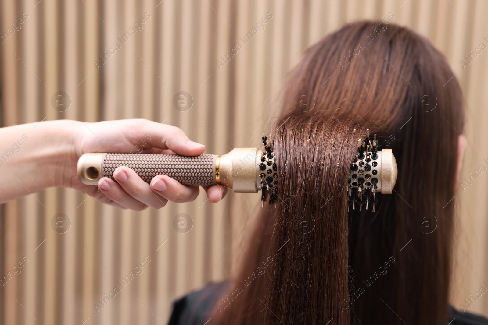 Photo of Hairdresser styling client's hair with round brush in salon, closeup