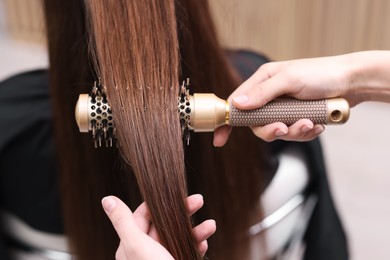 Photo of Hairdresser styling client's hair with round brush in salon, closeup