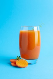 Photo of Fresh carrot smoothie in glass and cut vegetable on light blue background