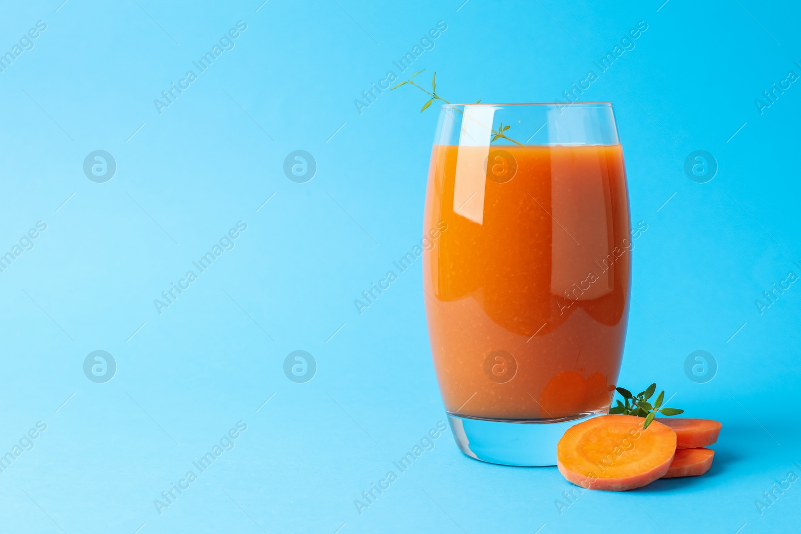 Photo of Fresh carrot smoothie in glass and cut vegetable on light blue background, closeup. Space for text