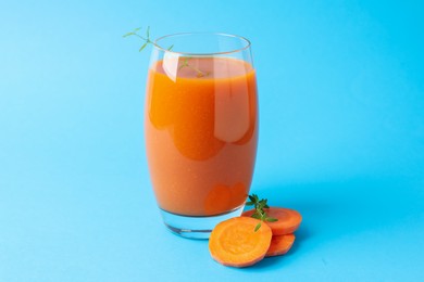 Photo of Fresh carrot smoothie in glass and cut vegetable on light blue background, closeup