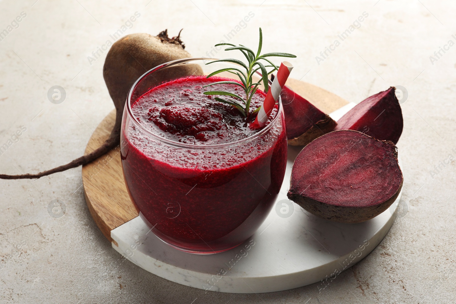 Photo of Fresh beetroot smoothie with rosemary in glass and cut vegetable on light textured table, closeup