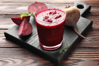 Photo of Fresh beetroot smoothie in glass and cut vegetable on wooden table, closeup