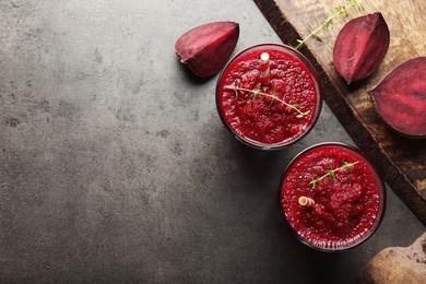 Photo of Fresh beetroot smoothie in glasses and cut vegetables on grey textured table, flat lay. Space for text