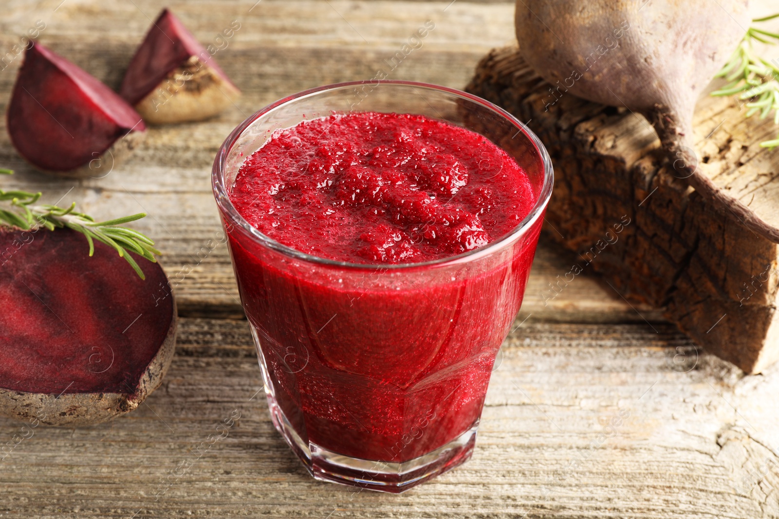 Photo of Fresh beetroot smoothie in glass, rosemary and cut vegetables on wooden table, closeup