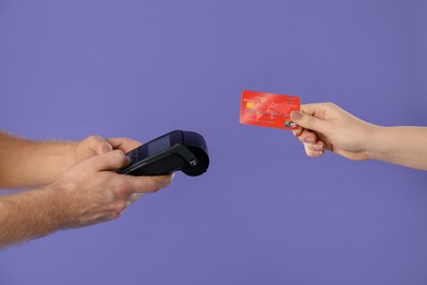 Photo of Man taking payment from client via terminal on purple background, closeup