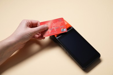 Photo of Woman with credit card using payment terminal on beige background, closeup