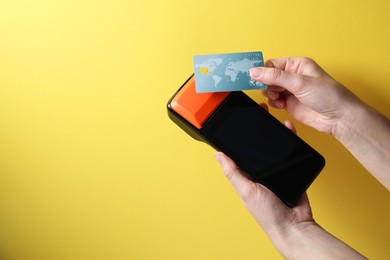 Photo of Woman with credit card using payment terminal on yellow background, closeup. Space for text