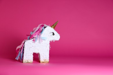 Photo of Unicorn shaped pinata on bright pink background, space for text