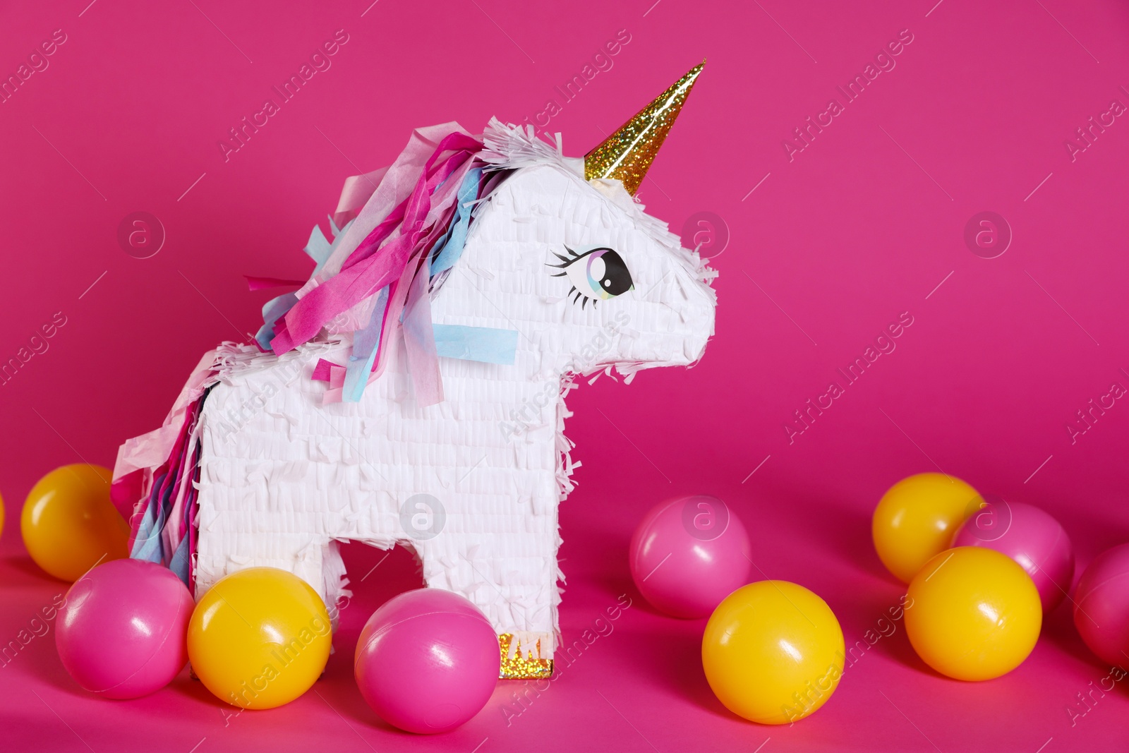 Photo of Unicorn shaped pinata and balls on bright pink background