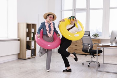 Happy colleagues with different beach accessories having fun in office