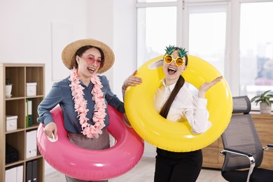 Happy colleagues with different beach accessories having fun in office