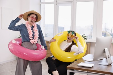 Happy colleagues with different beach accessories having fun in office