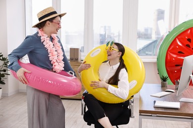 Happy colleagues with different beach accessories having fun in office