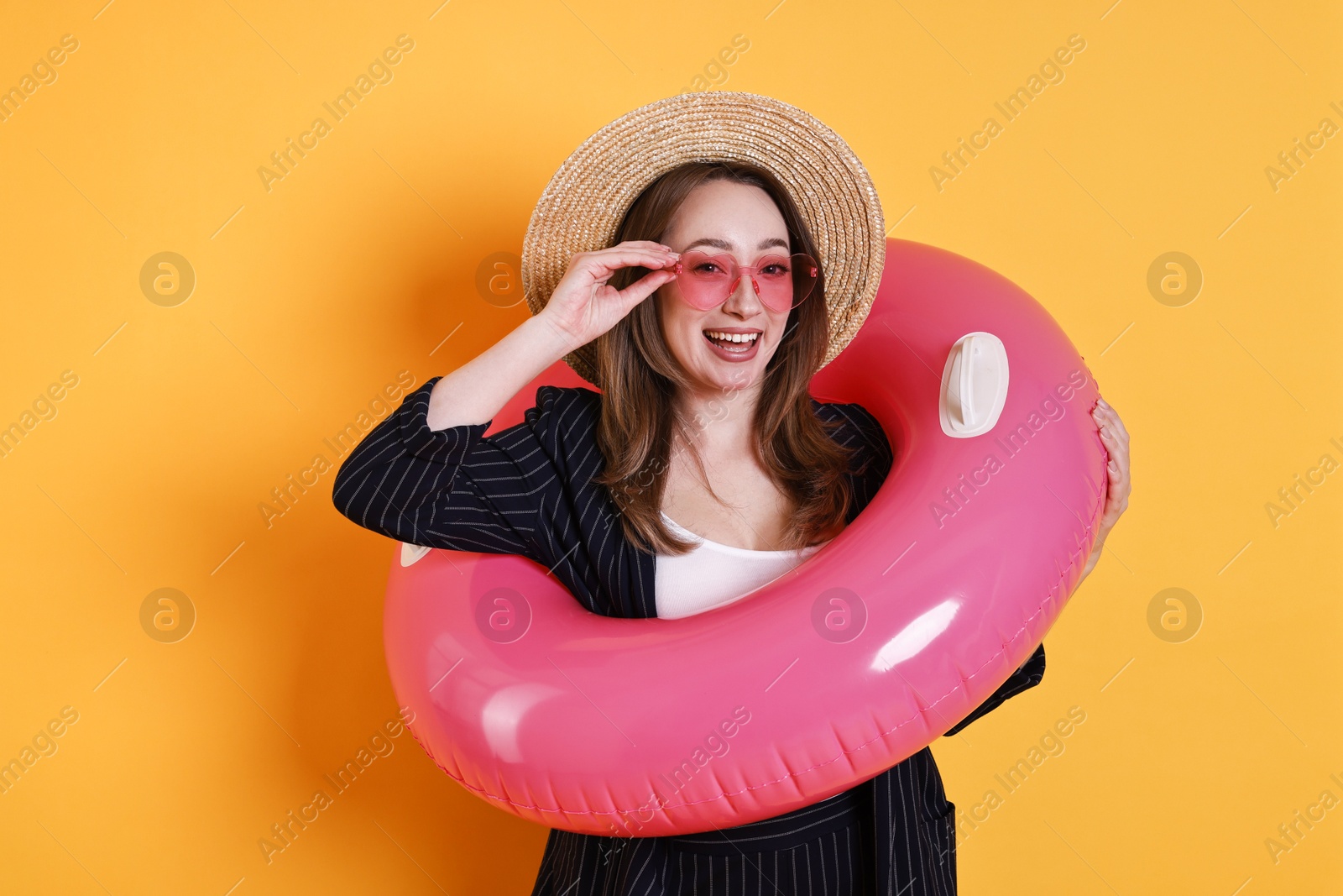 Photo of Businesswoman with inflatable ring, straw hat and sunglasses on orange background