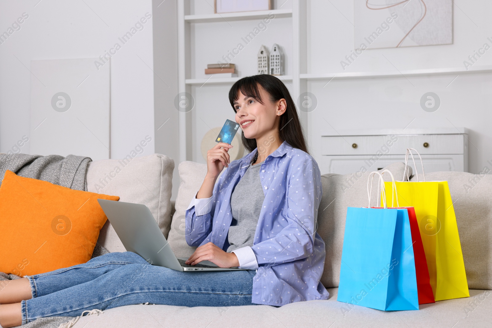 Photo of Internet shopping. Happy woman with credit card, laptop and colorful bags on sofa at home