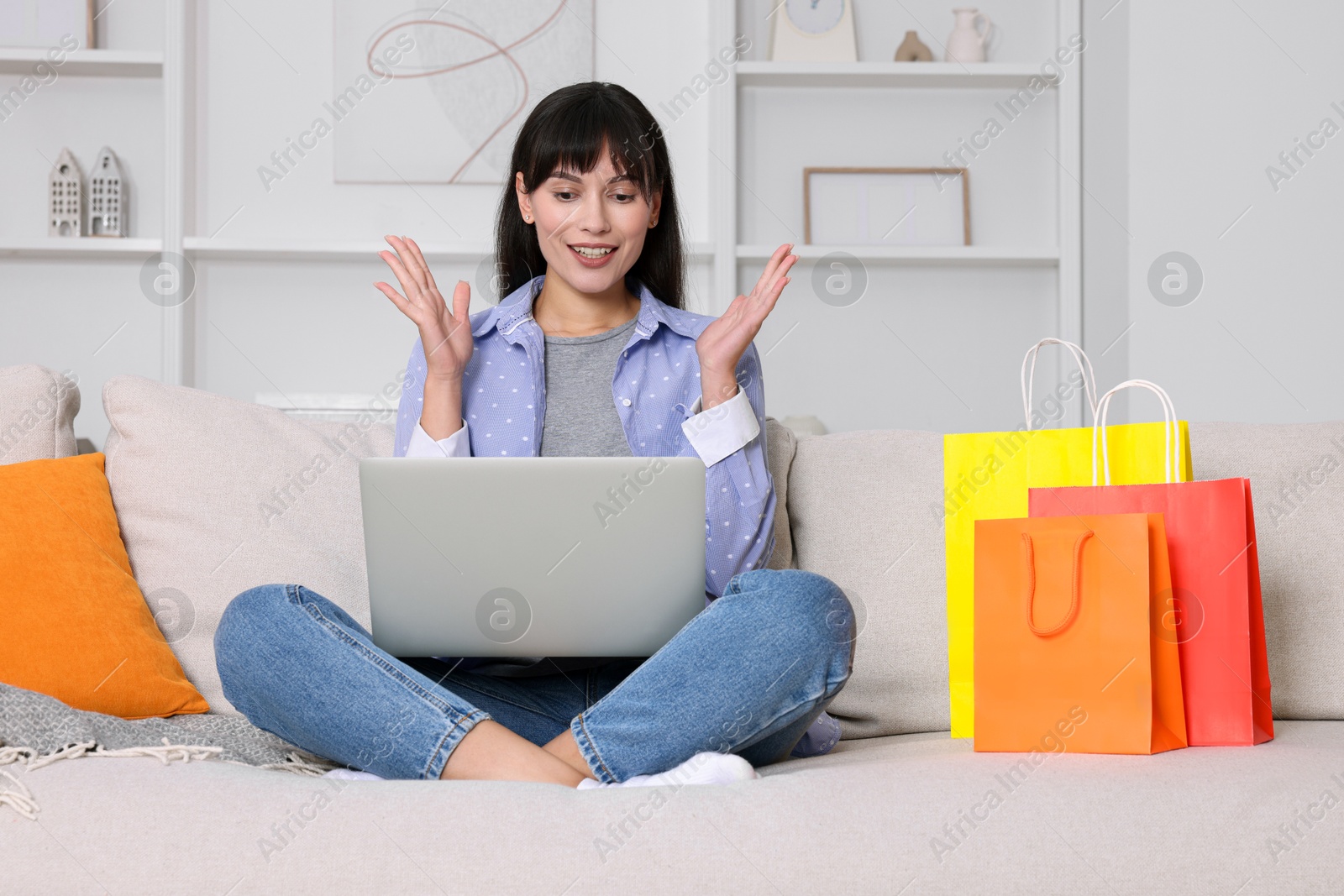 Photo of Internet shopping. Happy woman with laptop and colorful bags on sofa at home