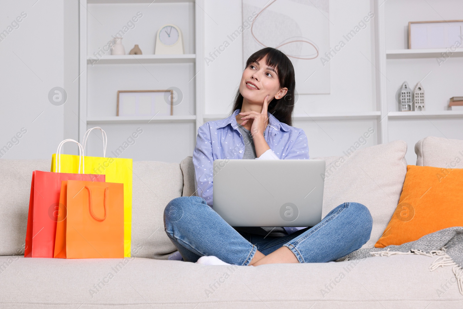 Photo of Internet shopping. Happy woman with laptop and colorful bags on sofa at home