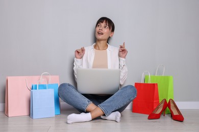 Photo of Internet shopping. Beautiful woman with laptop and colorful bags sitting near grey wall