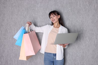 Internet shopping. Happy woman with laptop and colorful bags near grey wall