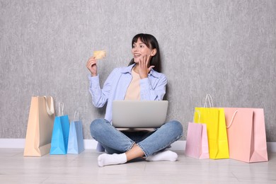 Photo of Internet shopping. Happy woman with credit card, laptop and colorful bags sitting near grey wall