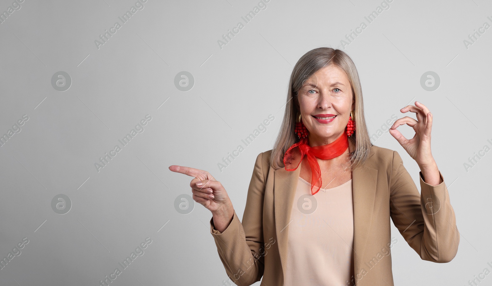 Photo of Senior woman showing okay gesture while pointing at something on light grey background