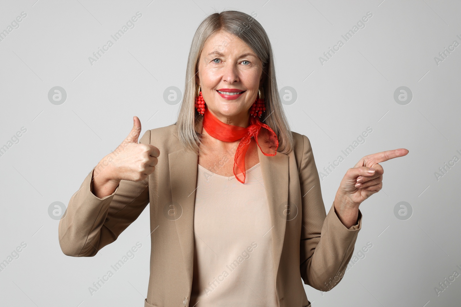 Photo of Senior woman showing thumbs up while pointing at something on light grey background