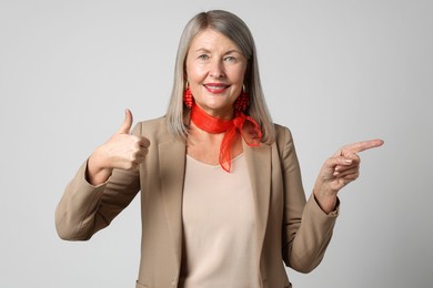 Photo of Senior woman showing thumbs up while pointing at something on light grey background