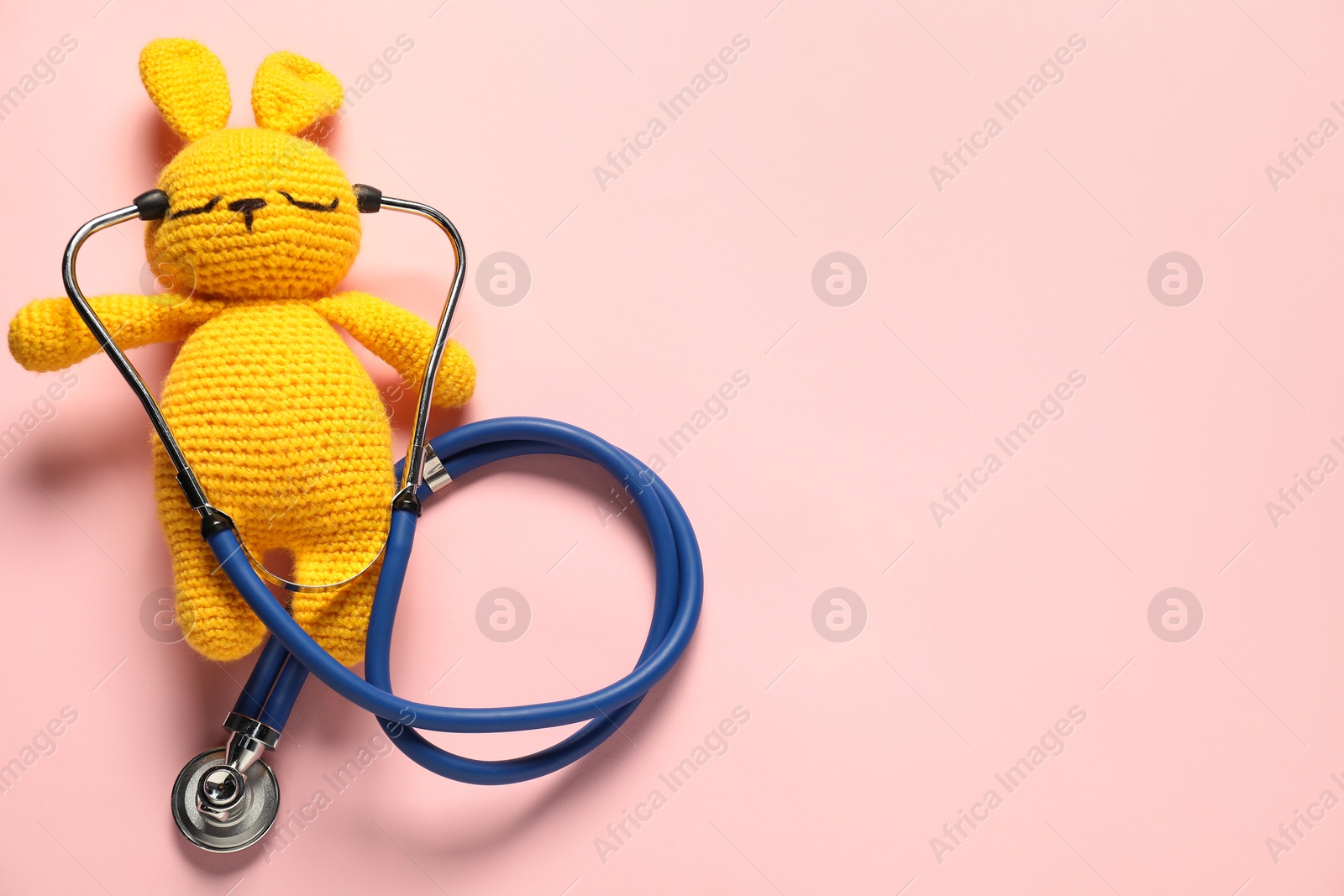 Photo of Pediatrics concept. Toy bunny with stethoscope on pink background, top view. Space for text