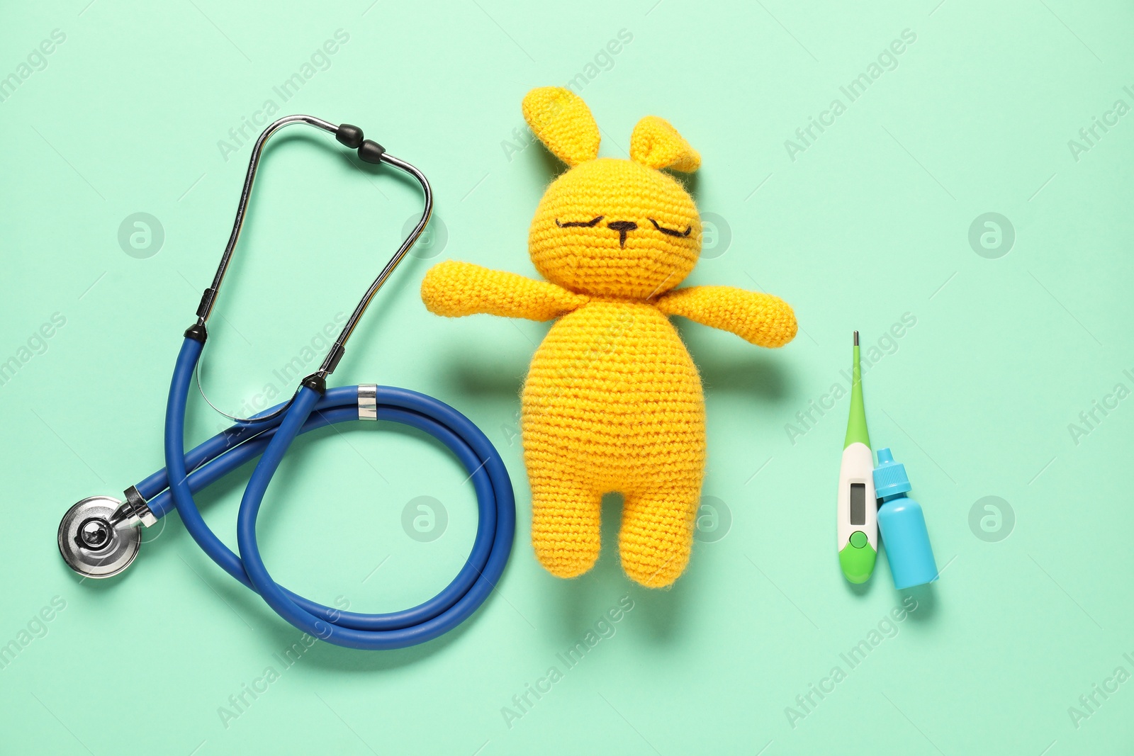 Photo of Pediatrics concept. Toy bunny with stethoscope, nasal spray and thermometer on turquoise background, flat lay