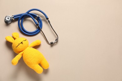 Photo of Pediatrics concept. Toy bunny with stethoscope on beige background, top view. Space for text