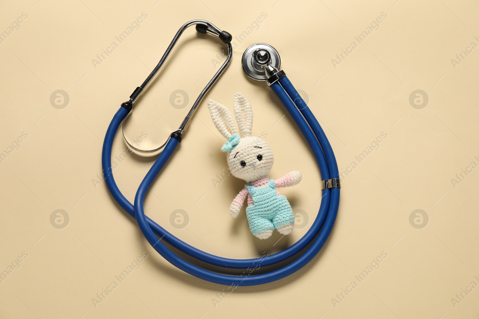 Photo of Pediatrics concept. Toy bunny with stethoscope on beige background, top view