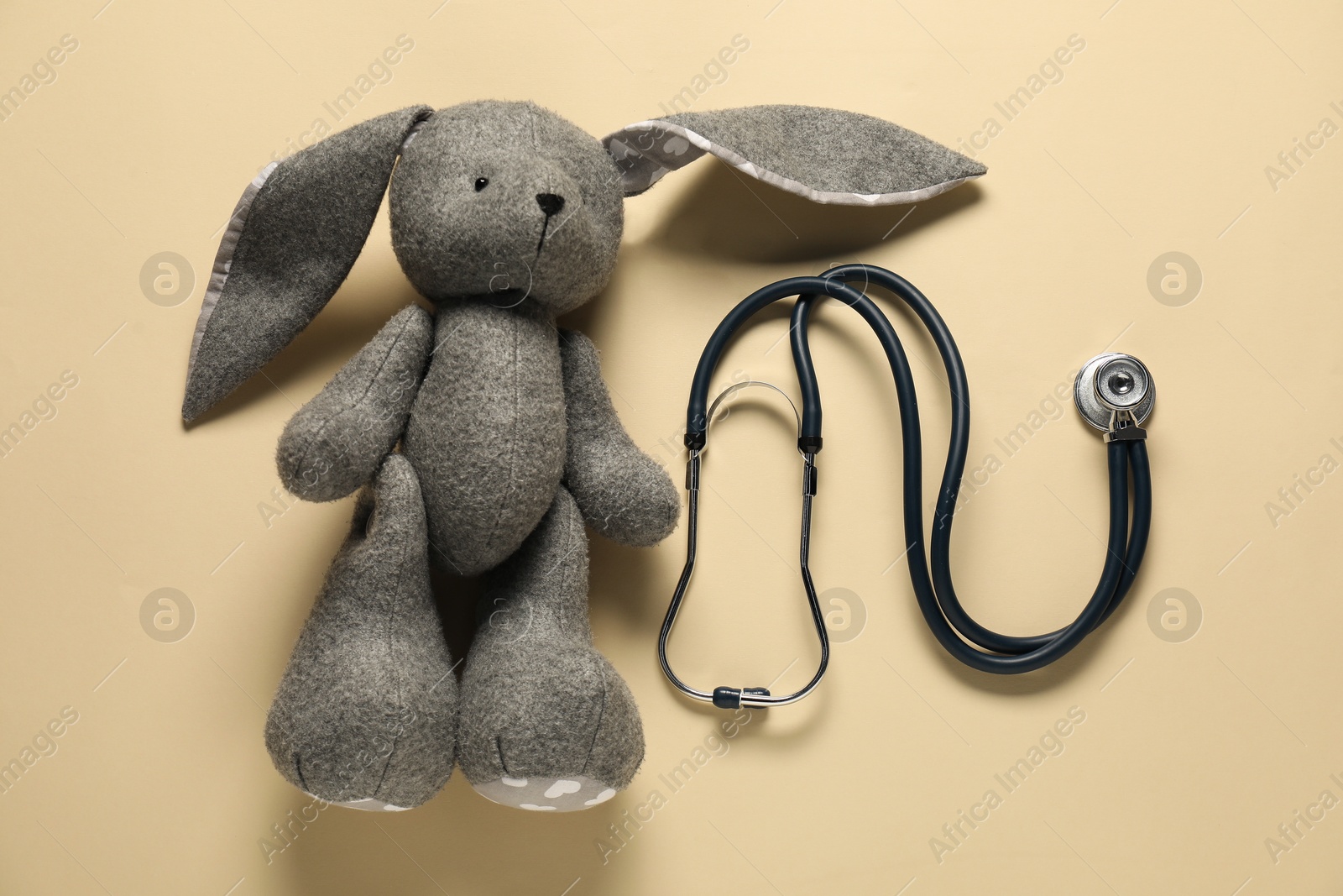 Photo of Pediatrics concept. Toy bunny with stethoscope on beige background, top view