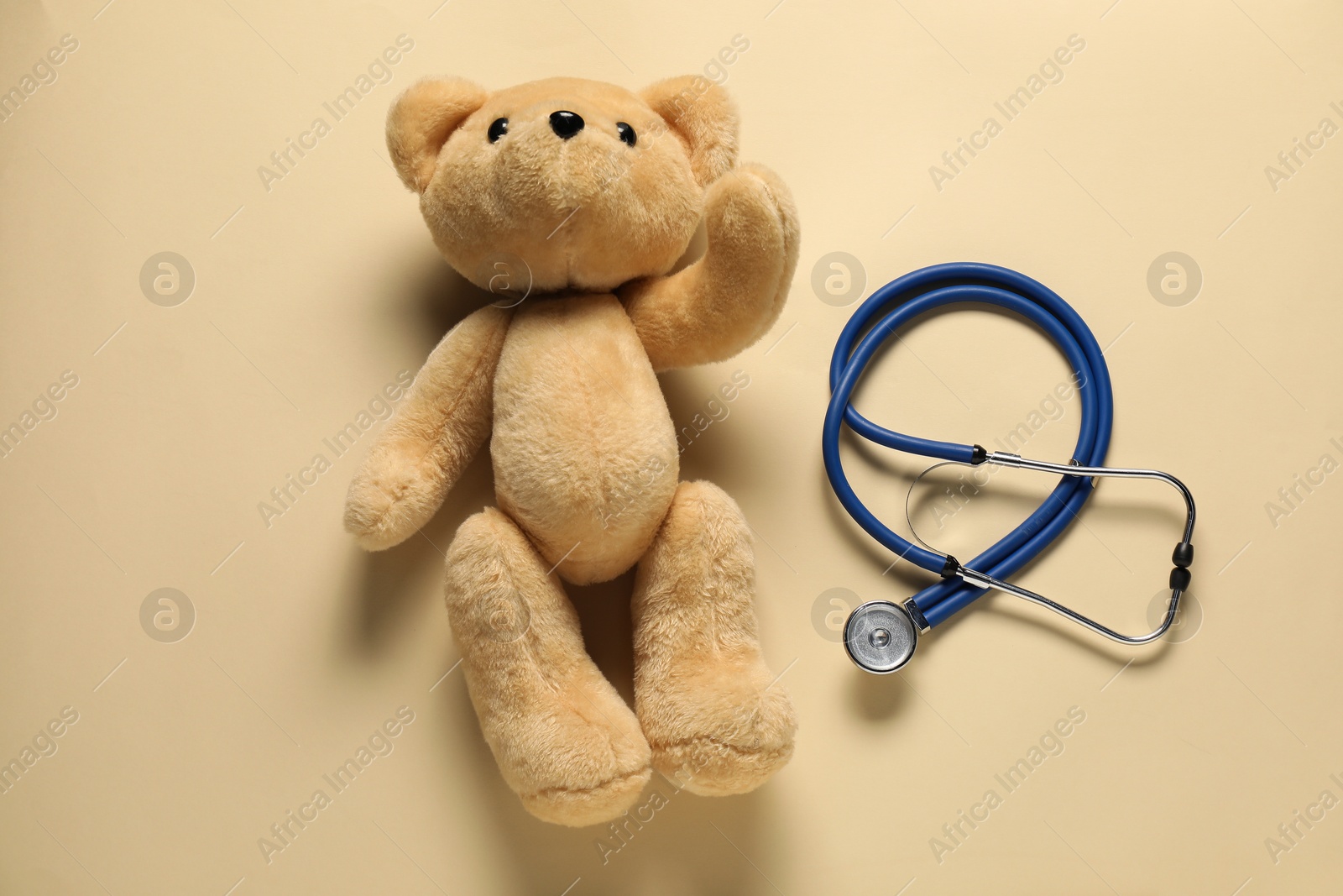 Photo of Pediatrics concept. Teddy bear with stethoscope on beige background, top view