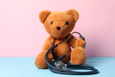 Photo of Pediatrics concept. Teddy bear with stethoscope on light blue wooden table against pink background