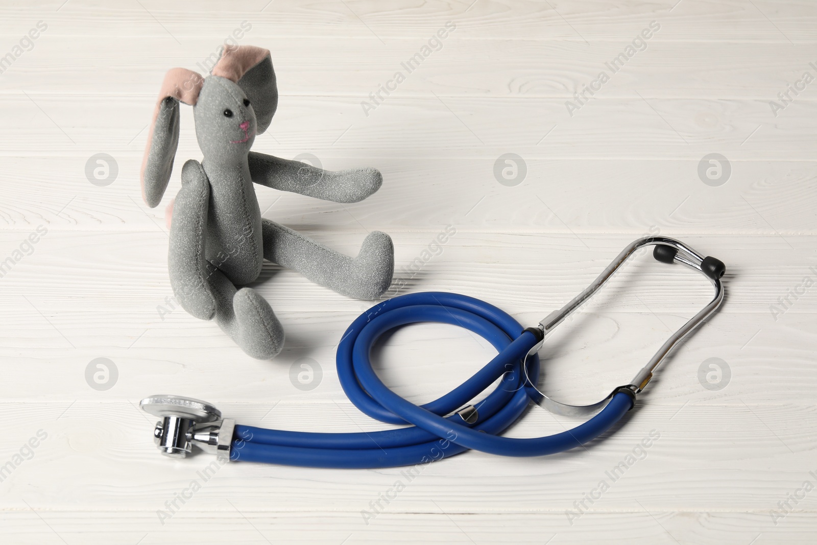 Photo of Pediatrics concept. Toy bunny and stethoscope on white wooden table